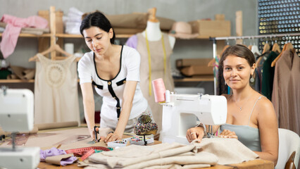 Woman fashion designer cutting a piece of paper before sewing, and dressmaker carefully sewing on a machine in the workshop