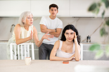 Domestic quarrel - offended young woman sits at the table while mother and young husband yell at her