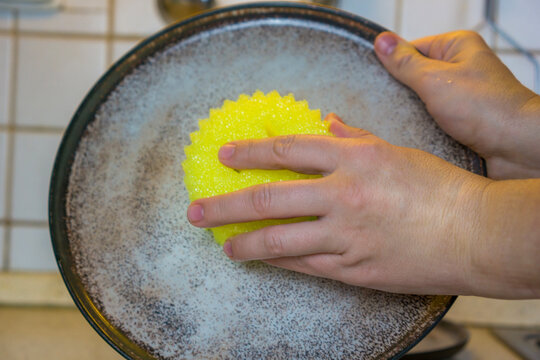 Womens hands scrubbing dirty speckled plate with bright yellow sponge in kitchen sink concept of daily chores, cleaning products, household routines