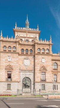 Panorama showing Cavalry Academy facade timelapse in Plaza de Zorrilla, Valladolid, Spain. Historic military building with intricate architecture, surrounded by busy urban scene under blue cloudy sky