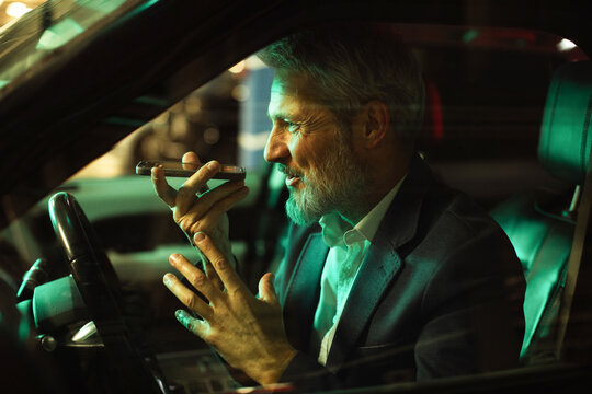 Mature businessman focused, talking on smartphone in car at night - Powered by Adobe