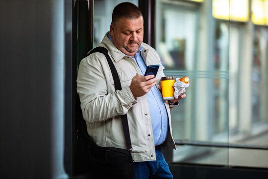 Adult man focused on smartphone with coffee at train station - Powered by Adobe