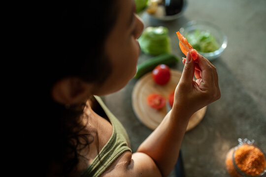 Young adult woman tasting tomato slice in home kitchen, focused