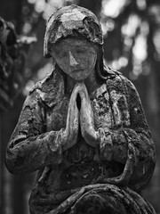 Weathered praying stone statue at Goat Gate Cemetery in Bratislava, captured in dramatic black and white.