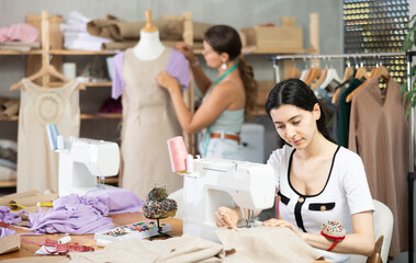 Team of dressmakers works on ordering clothes from a sewing workshop. Fashion designer checks the...