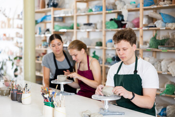 Young man in apron modeling clay pottery in workshop