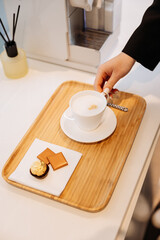 Cappuccino on wooden tray with chocolates, female hand, office coffee break scene