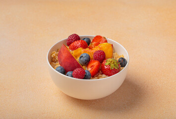 Oatmeal in white bowl topped with fresh peach slices, blueberries, strawberries, and raspberries, a nutritious and vibrant breakfast, promoting healthy eating habits