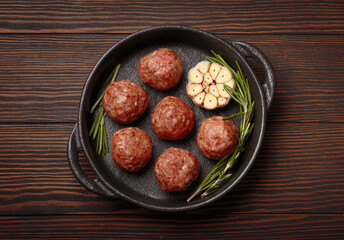 Raw meatballs seasoned with garlic and rosemary ready to be cooked in a cast iron pan, on a dark wooden table