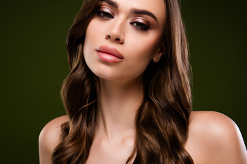 Naklejka premium Portrait of a young woman with flawless skin and brown wavy hair against a dark green backdrop