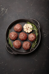 Raw meatballs seasoned with rosemary and garlic are waiting to be cooked in a cast iron pan top view on rustic dark background