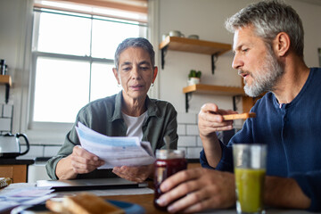 Mature couple reviewing bills with concerned expressions in home kitchen