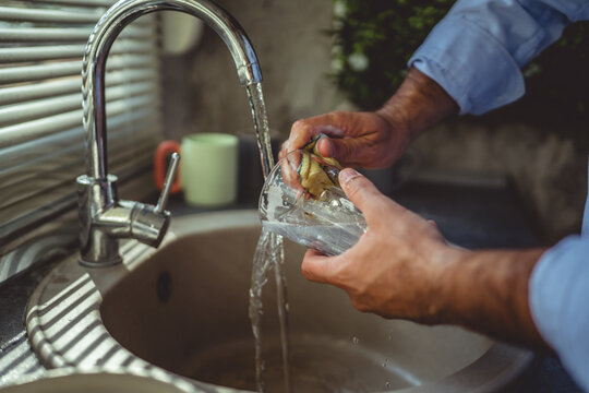 Man washing glass under running water in kitchen sink - Powered by Adobe
