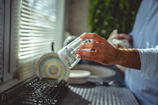 Man drying a clean glass in kitchen sunlight