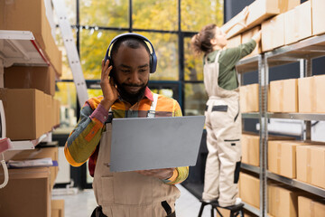 Black male staff enjoying depot work with music on headphones, handling operations in a small-scale...