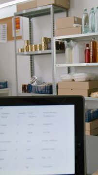 Vertical shot of tablet with customer order on associates counter at dark store, groceries, preserves, bottles of drinks, boxes with various food products on shelves