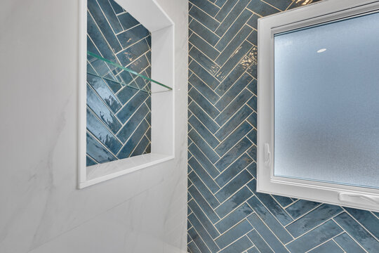 Stylish bathroom niche with glass shelves and herringbone tile accent wall.