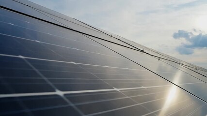 Low angle close-up of a large array of photovoltaic solar panels installed on a roof against a cloudy sky with bright sunlight - Powered by Adobe