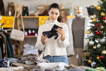 Armenian woman stands in a store decorated for Christmas and chooses stylish black heeled ankle boots. Woman on Christmas sale at clothing and shoe store.