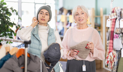 Elderly and young women buyers choosing warm hat in clothing store