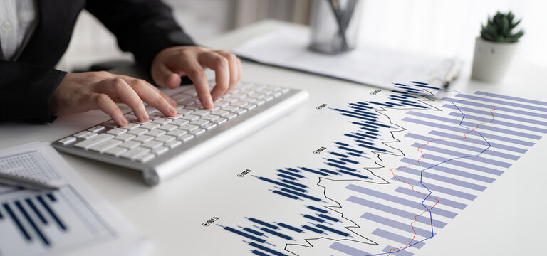A business professional engages with financial data on a modern keyboard amidst stock charts, showcasing a focused workspace designed for analysis and decision-making. Scalp