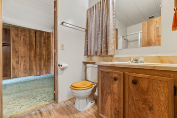 A bathroom with a toilet, sink, mirror, and wood cabinets