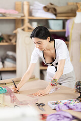Fototapeta premium Armenian woman works as a fashion designer in a sewing workshop and draws patterns for clothes using curved rulers