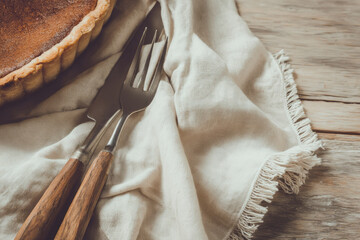 Minimal flat lay of dessert fork, knife, napkin, and pastry on rustic wooden table, warm soft lighting creates cozy inviting atmosphere for homemade baking enjoyment