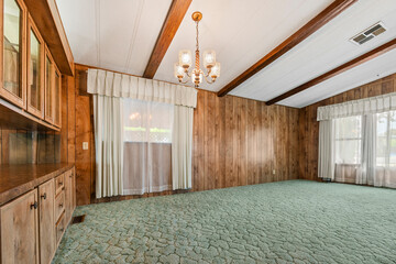 An empty living room with wood paneling, green carpet, and chandelier
