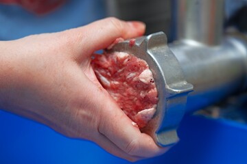 Woman's hand trying to unscrew a meat grinder plate clogged with meat tendons and gristle