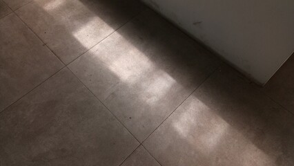 Minimalist abstract background showing a pattern of diagonal sunlight and sharp shadows across neutral-toned square tiled floor