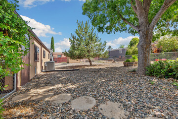 A gravel yard featuring a tree along with a house in the background