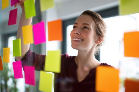 Creative businesswoman brainstorming ideas with colorful sticky notes on glass wall for innovative project planning in modern office setting