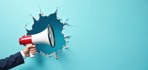 Businessman hand holds megaphone through torn blue wall. Hand in suit sleeve speaks through loudspeaker. Advertising and announcement concept with copy space.