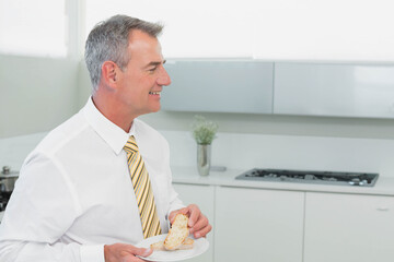Man wearing white shirt and yellow tie standing in modern kitchen holding pastry plate, copy space
