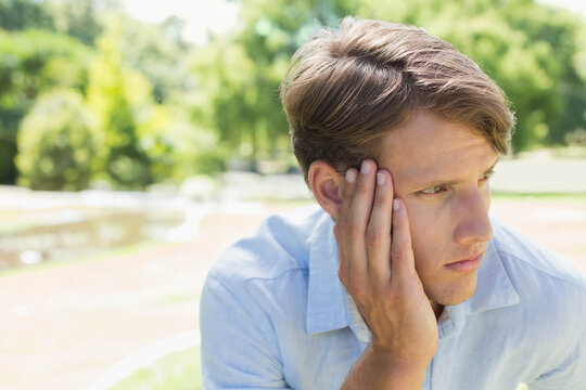 Adult man sitting on park bench wearing light blue collared shirt, resting hand, looking right