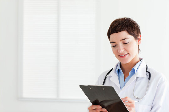 Mid-adult female physician using clipboard at clinic wearing lab coat and stethoscope, copy space