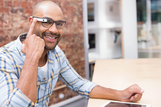 Mid adult man in plaid shirt tapping AR-display on glasses, sitting at loft table with tablet