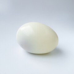 Peeled boiled egg in isolated white. A white boiled egg rests on a smooth, light grey surface. Its shiny, smooth texture and oval shape are clearly visible, highlighting the simplicity of the food