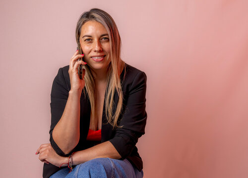 Businesswoman in a medium shot holding a phone to her ear, smiling at the camera confidently against a warm background.