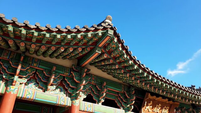 4k shot of an ornate Korean temple roof featuring intricate patterns and vibrant colors under a clear blue sky, showcasing architectural detail in a horizontal