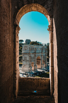 The Arch of Constantine framed perfectly through a dark, weathered brick archway of the Colosseum ruins. Vertical shot.