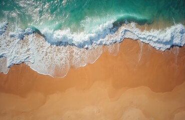 Ocean waves crash on a golden sand beach, seen from above. Turquoise water meets the shore, creating white foam patterns. Ideal for summer travel, nature, or relaxation themes.