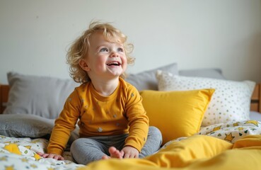 Blond toddler boy wakes up smiling in bed. Happy child sits up under yellow and white star patterned duvet. Kid rests comfortably on pillows with soft morning light.