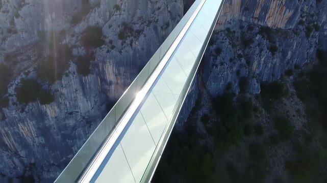 A transparent bridge spans a chasm between rocky cliffs, bathed in sunlight