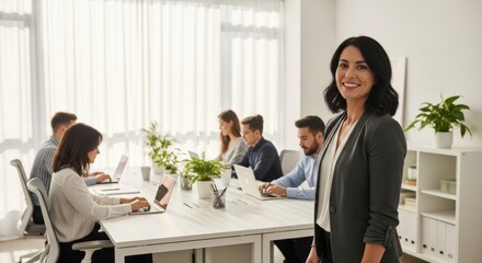 Smiling woman in business attire stands in front of a meeting with coworkers at a long white table
