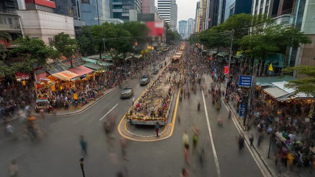 A bustling city street filled with a large crowd and a parade float, captured with motion blur during an urban event.