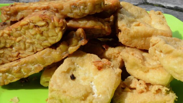 Extreme Close-up of Crispy Fried Tofu (Tahu) and Tempeh Served on a Bright Green Plate. Traditional Indonesian Vegan Food, Plant-Based Protein, and Street Food