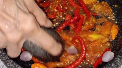 A hand grinds fresh ingredients—red chilies, shallots, garlic, shrimp paste, salt, and tomato—meticulously in a stone mortar (cobek).