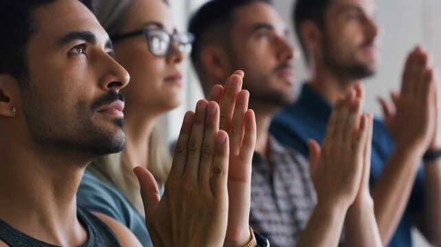 A group of diverse people with hands clasped together, looking attentively forward in a respectful or meditative pose.